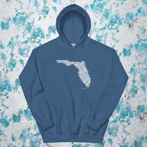 May include: A blue hooded sweatshirt featuring a white outline of the state of Florida. The outline is filled with various white illustrations. The sweatshirt has a front pocket and a drawstring hood.