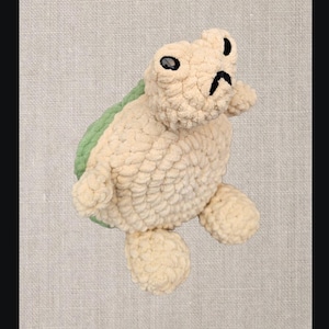 May include: A plush, cream-colored turtle with a green shell. The turtle has black eyes and a black mouth. The words "NEW IN" are repeated at the top and bottom of the image.