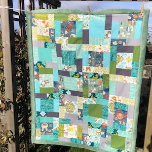 May include: A patchwork quilt with a variety of fabric patterns and colors, including teal, green, gray, and white. The quilt features woodland animal and leaf designs. The edges are finished with a soft green border.