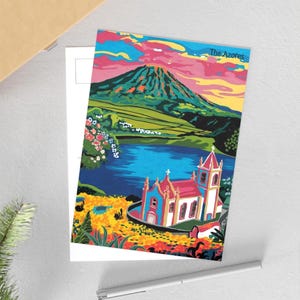 Peut inclure: Une carte postale colorée représentant un paysage des Açores. L'image montre une montagne, un lac et une église. Le texte "The Azores" est visible. La carte postale est posée sur une carte blanche.
