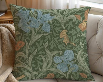May include: A square throw pillow featuring a dark olive green background with a repeating pattern of light blue iris flowers, orange blossoms, and a small tan bird perched among dense, leafy green foliage and stems.