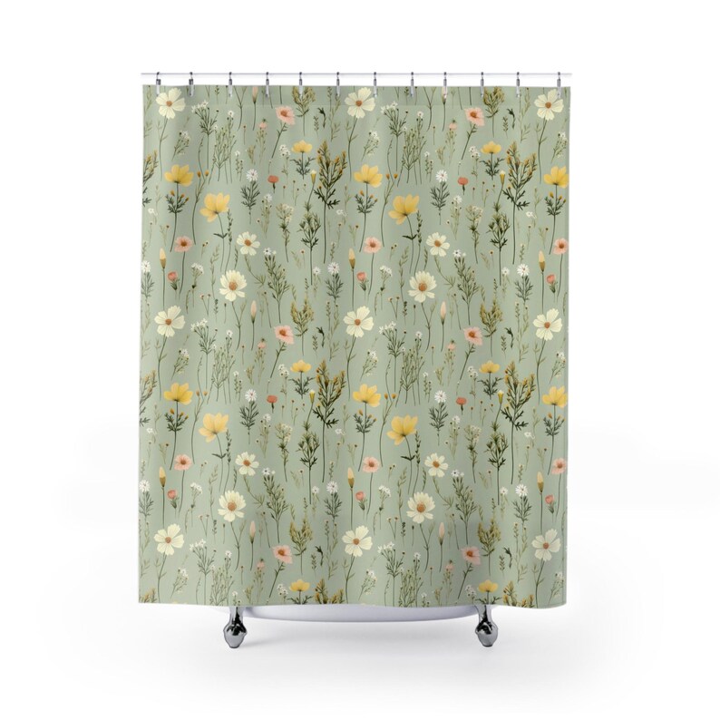 May include: A shower curtain featuring a repeating pattern of wildflowers in yellow, white, and pink against a muted green background. The floral design includes various types of flowers and foliage, creating a natural and whimsical aesthetic.