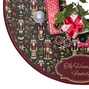 May include: A Christmas tree skirt with a dark green background featuring nutcracker soldiers, stars, and holly. The skirt has a maroon border and is decorated with gifts, pinecones, and a silver ornament. A gift box is tied with a red bow.
