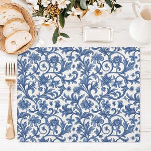 May include: A rectangular placemat with a blue floral pattern on a white background. The design features stylized flowers and leaves. A gold fork, a basket of bread, and a white pitcher are also visible.