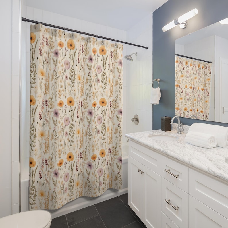 May include: A floral shower curtain with a cream background and a pattern of orange, purple, and yellow flowers and green foliage. The curtain is hanging in a bathroom with a white vanity and a mirror.