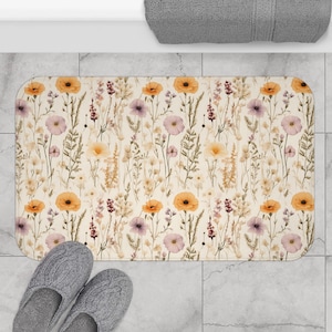 May include: A beige bath mat with a floral pattern featuring yellow and purple flowers on a white background.