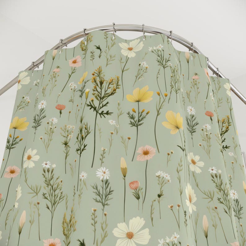 May include: A shower curtain with a floral pattern. The design features various wildflowers in shades of yellow, pink, and white against a soft green background. The curtain is hanging from a curved metal rod.