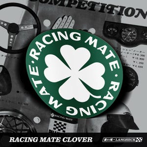 May include: A green and white Racing Mate Clover sticker with a four-leaf clover design. The sticker has the words "RACING MATE" in a circular pattern around the clover. The background features vintage racing equipment.