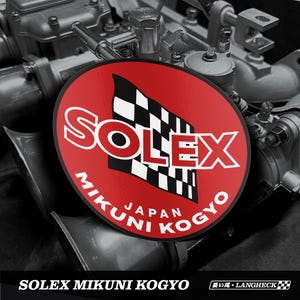 May include: A circular red Solex Mikuni Kogyo logo with a black and white checkered flag. The logo features white text and Japanese characters. The background is a monochrome image of an engine.