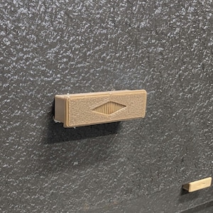 Pode incluir: Uma puxador de gaveta retangular marrom com um design em forma de diamante no centro.