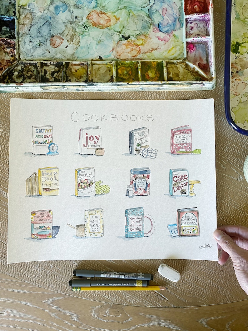 May include: A watercolor illustration of a collection of cookbooks with titles like "Salt Fat Acid Heat", "Joy of Cooking", "The Barefoot Contessa", "How to Cook Everything", "The Fannie Farmer Cookbook", "Mastering the Art of French Cooking", "Betty Crocker Picture Cookbook", "The Cake Doctor", and "Beard's American Cookery".