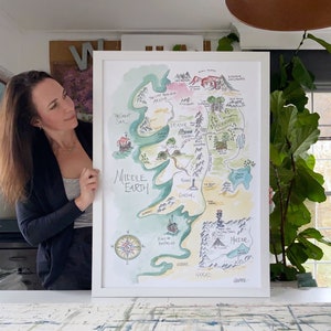 Puede incluir: Una pintura de acuarela de un mapa de la Tierra Media, una tierra ficticia de los libros de El Se&ntilde;or de los Anillos. El mapa est&aacute; enmarcado en blanco y est&aacute; colgado en una pared. El mapa muestra las diferentes regiones de la Tierra Media, incluyendo la Comarca, Mordor y Gondor.