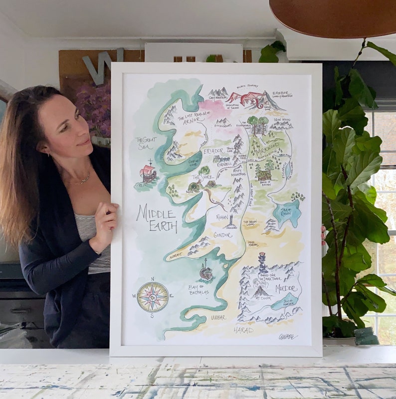 Puede incluir: Una pintura de acuarela de un mapa de la Tierra Media, una tierra ficticia de los libros de El Se&ntilde;or de los Anillos. El mapa est&aacute; enmarcado en blanco y est&aacute; colgado en una pared. El mapa muestra las diferentes regiones de la Tierra Media, incluyendo la Comarca, Mordor y Gondor.