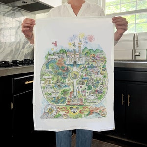 May include: A white tea towel with a hand-drawn map of Disneyland. The map shows the different lands, including Fantasyland, Tomorrowland, and Adventureland. The map is surrounded by fireworks and a Mickey Mouse head.