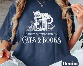 Può includere: T-shirt blu navy con grafica bianca di un gatto sui libri, con la scritta "EASILY DISTRACTED BY CATS & BOOKS". La maglietta ha una vestibilità ampia ed è realizzata in materiale morbido.