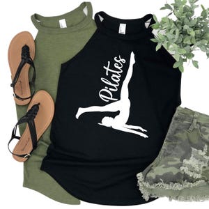 May include: A black Pilates tank top with a white graphic of a person doing a Pilates pose. The tank top is next to an olive green tank top, a pair of brown sandals, and camouflage shorts.