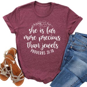 May include: A maroon t-shirt with a white graphic that reads "She is far more precious than jewels Proverbs 31:10".