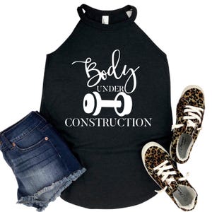 May include: A black tank top with the text "Body Under Construction" and a dumbbell graphic. The image also includes denim shorts and leopard print sneakers.