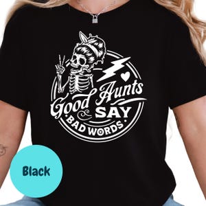 May include: Black t-shirt with a white graphic featuring a skeleton with a peace sign, a lightning bolt, and the words "Good Aunts Say Bad Words." A light blue circle with the word "Black" is in the lower left.