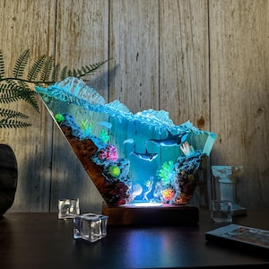 May include: A decorative resin sculpture depicting an underwater scene with orcas, coral, and other marine life. The sculpture is illuminated with blue light, creating a vibrant and captivating display. The base is made of wood.