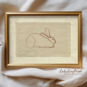 Könnte beinhalten: Eine gerahmte Vintage-Skizze eines Kaninchens in einem goldenen Rahmen. Die Skizze ist eine einfache Strichzeichnung in brauner Tinte auf beigem Hintergrund. Der Rahmen ist rechteckig und hat eine goldene Oberfläche. Der Text "Lady Luxy Prints" ist sichtbar.