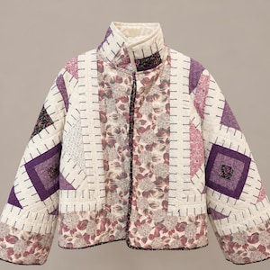 May include: A quilted jacket featuring a patchwork design with cream, purple, and floral fabric panels. The garment has a high collar, long sleeves, and visible stitching throughout, combining solid cream sections with patterned purple and floral prints.