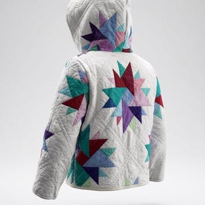 May include: A quilted jacket with a hood, featuring a white background and colorful star patterns in shades of red, blue, purple, and teal. The jacket has a diamond-stitched pattern and a relaxed fit.