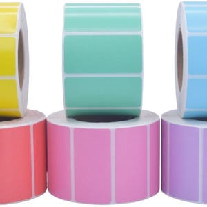 Puede incluir: Una colección de rollos de etiquetas coloridas. La imagen muestra rollos de etiquetas amarillas, turquesas y azules apilados sobre rollos de etiquetas rojas, rosas y moradas. Cada etiqueta es rectangular con esquinas redondeadas.