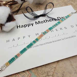 May include: A handmade beaded bracelet with a silver clasp. The bracelet features a pattern of teal, gold, and peach-colored beads. The text "Happy Mothers Day" is visible on a white card. The bracelet is made by CandraElla.