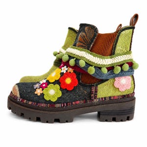 May include: An ankle boot featuring a dark gray toe and heel, a lime green side panel, and a brown ribbed elastic insert. The boot is decorated with colorful crocheted flower appliqués, a braided trim, and a row of small green pom-poms.