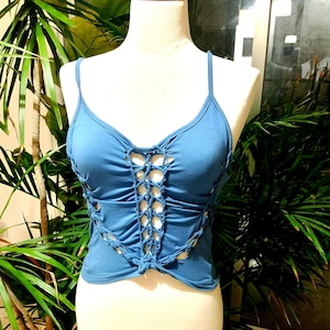 Può includere: Canotta azzurra con spalline sottili e un design traforato unico. La parte anteriore presenta un motivo a griglia centrale e tagli laterali, creando un look elegante e moderno. La canotta è esposta su un manichino.