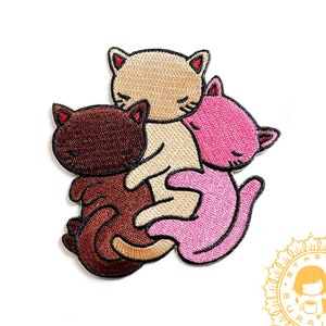 Può includere: Toppa ricamata termoadesiva con tre gatti stilizzati marroni, beige e rosa. La toppa presenta il testo "neapolitan kitties" e "embroidered iron-on patch" in arancione. È visibile anche il sito web stasiaburrington.com.