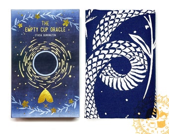 May include: The Empty Cup Oracle deck with a navy blue background and gold accents. The front of the box features a circular design with a moth and the text "The Empty Cup Oracle" and "Stasia Burrington". The other side has a white and navy blue snake design.
