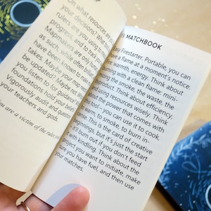 May include: Open pages of a book titled "The City of Oracle" with text about "Map" and "Matchbook". The pages are held open by a hand with a gold ring. The background is a light, glittery surface.
