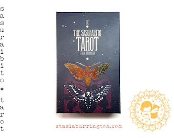 May include: The Sasuraibito Tarot card deck box. The box is dark with gold accents and features two moth illustrations. The text "THE SASURAIBITO TAROT" is displayed prominently. The artist's name, Stasia Burrington, is also visible.