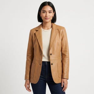 Può includere: Un blazer in pelle color cuoio con revers dentellato, due tasche frontali applicate e chiusura a due bottoni. La giacca è indossata sopra un top color crema e jeans blu scuro, caratterizzata da una vestibilità strutturata e maniche lunghe.