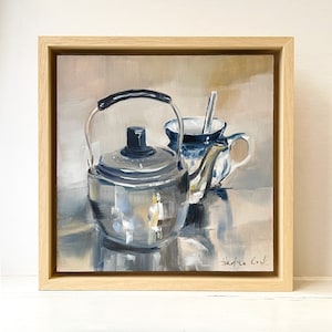 Könnte beinhalten: Ein Stillleben mit einer silbernen Teekanne und einer blau-weißen Keramik-Teetasse mit einem Löffel darin. Das Gemälde ist in einem hellen Holzrahmen gerahmt und trägt die Unterschrift des Künstlers unten rechts.