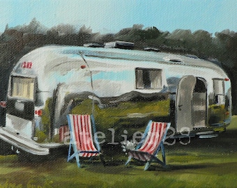 May include: A vintage silver Airstream trailer parked in a grassy field with two red and white striped beach chairs in front of it.