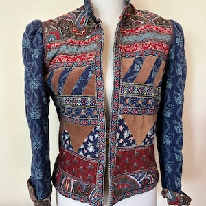May include: A blue quilted jacket with a patchwork design featuring paisley, floral, and geometric patterns in shades of red, brown, and blue.