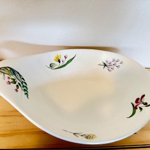 May include: A white, oval-shaped serving dish with a floral design. The dish features hand-painted flowers in yellow, purple, and red, with green leaves. The dish is made of ceramic and is suitable for serving appetizers or desserts.