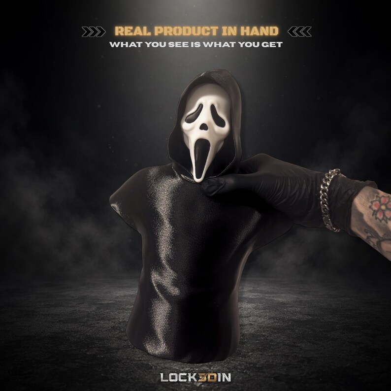 May include: A black hooded bust featuring a white ghost-like mask with hollow black eyes and an elongated open mouth. The text above reads REAL PRODUCT IN HAND WHAT YOU SEE IS WHAT YOU GET and the text below reads LOCK3DIN in white lettering.