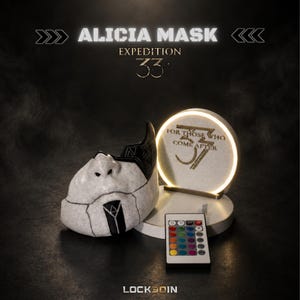 Peut inclure: Un masque blanc et noir avec des motifs géométriques, accompagné d'un présentoir circulaire lumineux portant le texte FOR THOSE WHO COME AFTER 33. Une télécommande multicolore est placée devant le présentoir.