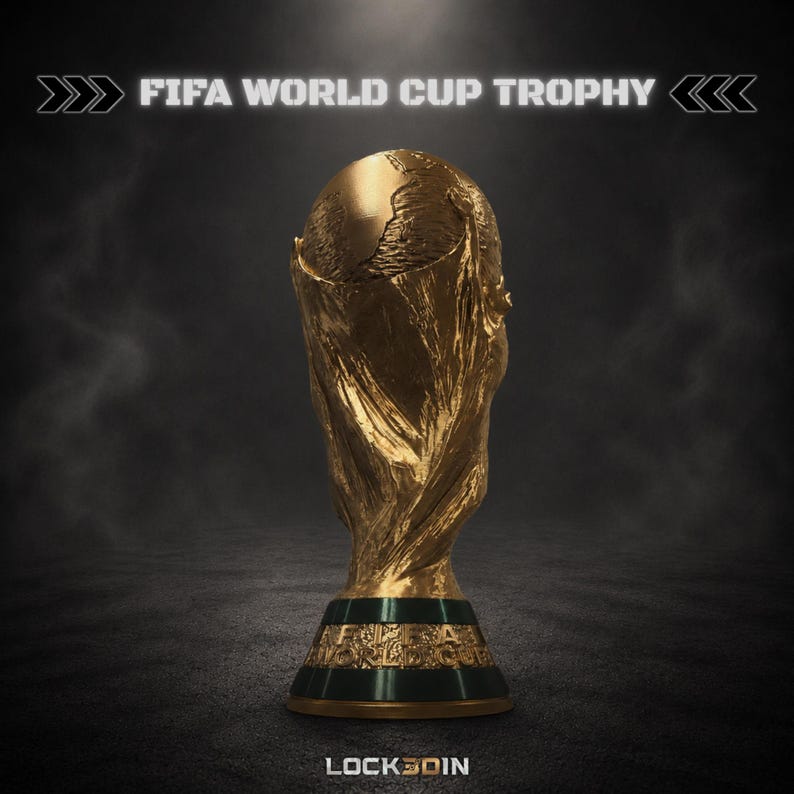 Peut inclure: Une r&eacute;plique dor&eacute;e du troph&eacute;e de la Coupe du Monde de la FIFA repr&eacute;sentant un globe soutenu par deux figures sur une base sombre avec le texte FIFA WORLD CUP TROPHY en haut et LOCK3DIN en bas. Le troph&eacute;e a une finition m&eacute;tallique textur&eacute;e.