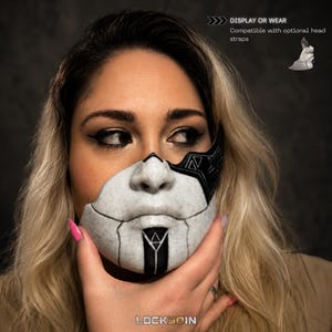 Puede incluir: Una m&aacute;scara facial blanca y negra con textura moteada y patrones geom&eacute;tricos. La m&aacute;scara cubre el &aacute;rea de la nariz y la boca, con una franja negra vertical central y un icono de tri&aacute;ngulo. Texto: DISPLAY OR WEAR Compatible with optional head straps.