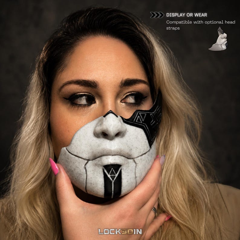 Puede incluir: Una m&aacute;scara facial blanca y negra con textura moteada y patrones geom&eacute;tricos. La m&aacute;scara cubre el &aacute;rea de la nariz y la boca, con una franja negra vertical central y un icono de tri&aacute;ngulo. Texto: DISPLAY OR WEAR Compatible with optional head straps.