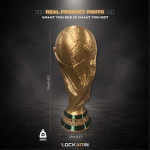 Peut inclure: Un troph&eacute;e de couleur dor&eacute;e repr&eacute;sentant un globe soutenu par deux figures, avec une bande verte &agrave; la base. Le texte indique : REAL PRODUCT PHOTO, WHAT YOU SEE IS WHAT YOU GET, 37cm (14.5"), 500G, 13cm (5.1"), et LOCK3DIN.