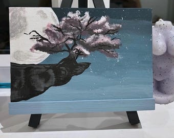 May include: A painting on canvas depicting a dark silhouette of a cliff with a pink and white flowering tree growing out of it. The background is a dark blue sky with a white moon and white stars.