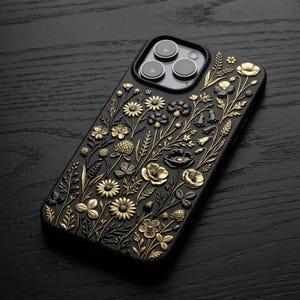 May include: Black phone case with a floral design. The case has an embossed pattern of various flowers and foliage in gold and black. The phone case is on a dark wood surface.