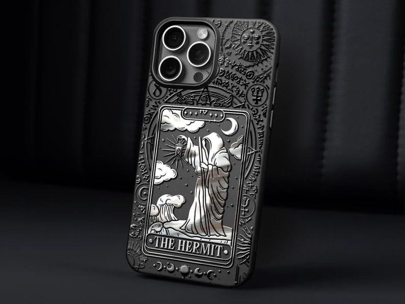 K&ouml;nnte beinhalten: Schwarze Handyh&uuml;lle mit detailliertem Pr&auml;gedesign. Sie zeigt eine Tarotkarten-Illustration von "Der Eremit" mit einer Kapuzenfigur, Wolken und einem Mond. Die H&uuml;lle hat eine strukturierte Oberfl&auml;che und aufwendige Bord&uuml;rendetails.