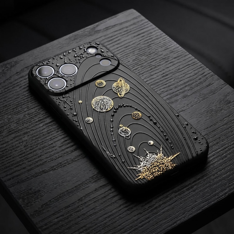 Peut inclure: Coque de t&eacute;l&eacute;phone noire avec un motif plan&eacute;taire d&eacute;taill&eacute; en or et argent. L'&eacute;tui pr&eacute;sente des &eacute;l&eacute;ments en relief et textur&eacute;s repr&eacute;sentant des plan&egrave;tes, des orbites et des corps c&eacute;lestes. L'&eacute;tui a une finition mate.